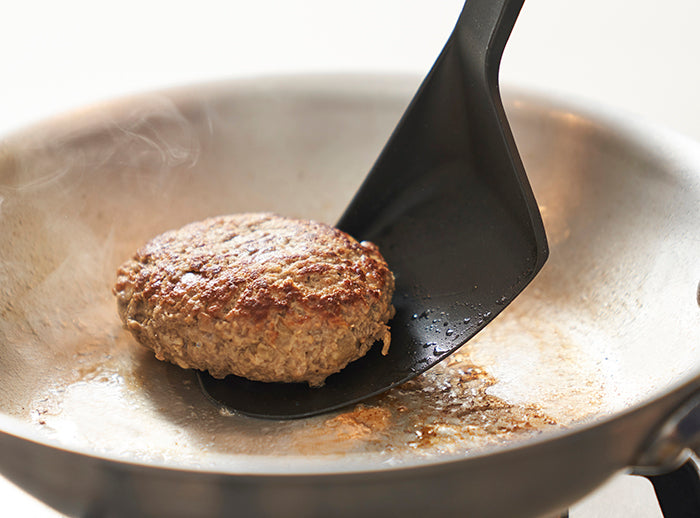 Spatula in use flipping a burger in a pan