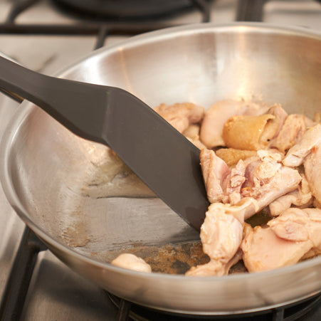 Spatula in use stir-frying chicken pieces in a pan