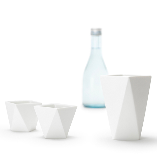 Shuki sake-kopjes van Alessi, wit keramisch, drie maten naast een fles