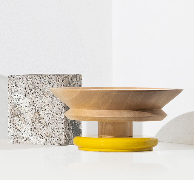 Zijaanzicht van de Alessi Twergi fruitschaal in blank hout met gele basis.
