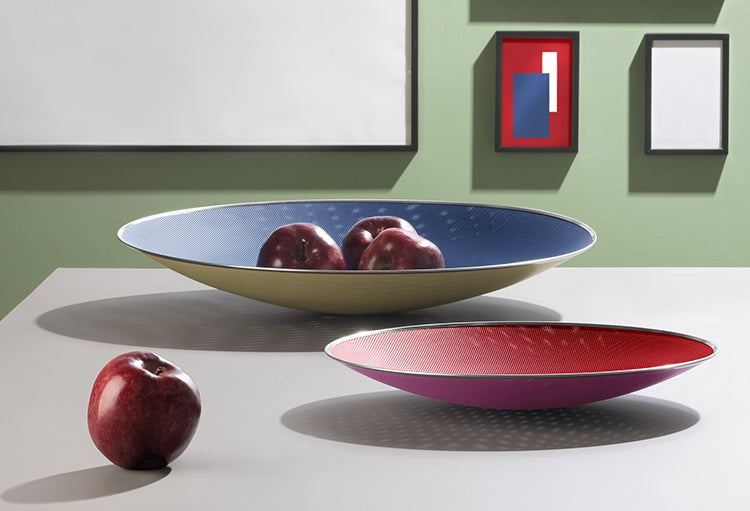 Twee Cohncave schalen van Alessi naast elkaar, in rood-paars en blauw-geel