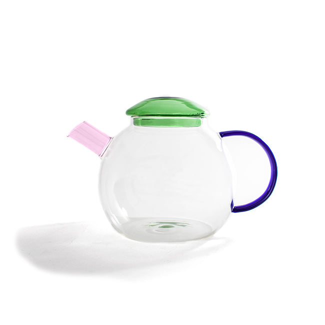Zijaanzicht van de glazen theepot met roze tuit en blauw handvat