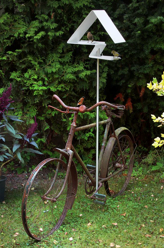 Wit vogelvoederhuis op stang bevestigd aan oude fiets in tuin