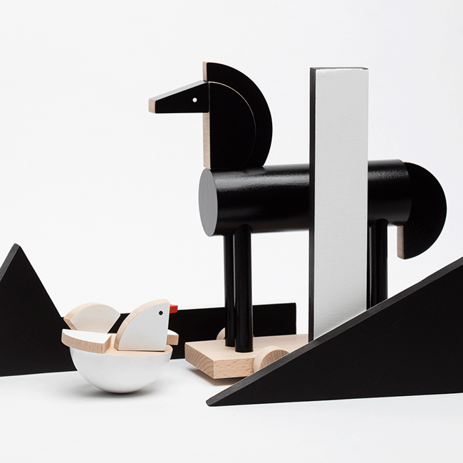 Zwarte houten paard op blank basis, naast de Holu; Alessi speelgoed, ontwerp Pavla Bohácová.