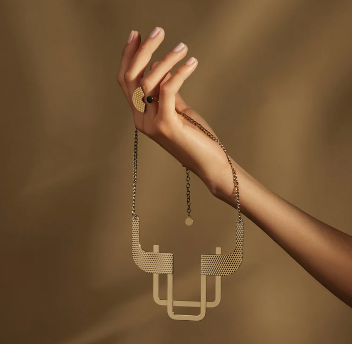 Trama halsketting van Alessi, ontwerp Elena Salmistraro, gouden band met geometrisch patroon, gedragen aan de hand