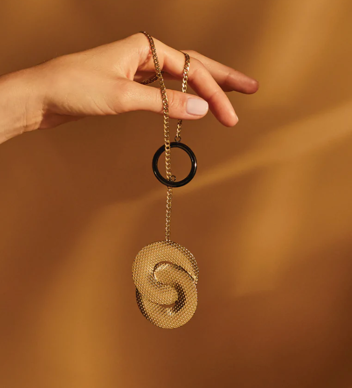 Alessi Acta halsketting met gouden band en zwarte ring, in de hand gehouden