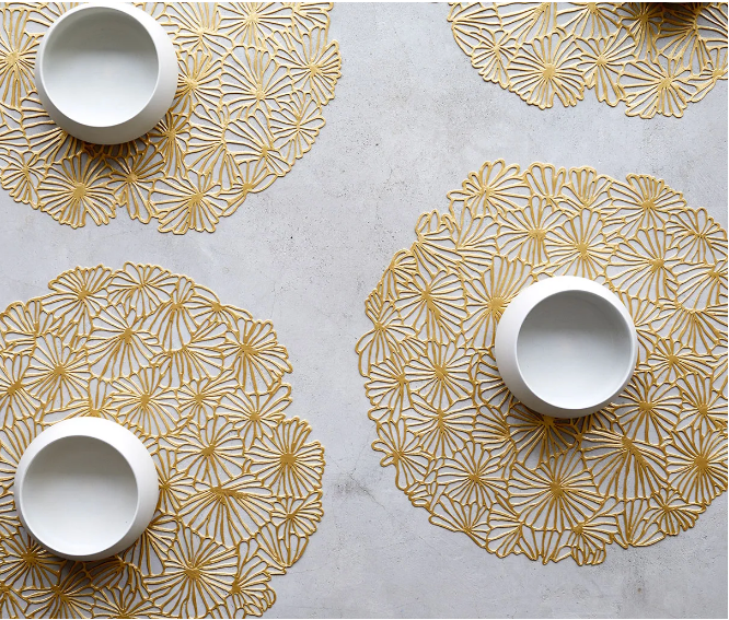 Vier mooie placemats met goudkleurig bloemmotief, elk met een witte schaal erop