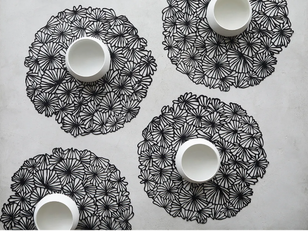 Vier Alessi Daisy placemats in zwart, elk met witte schaal erop