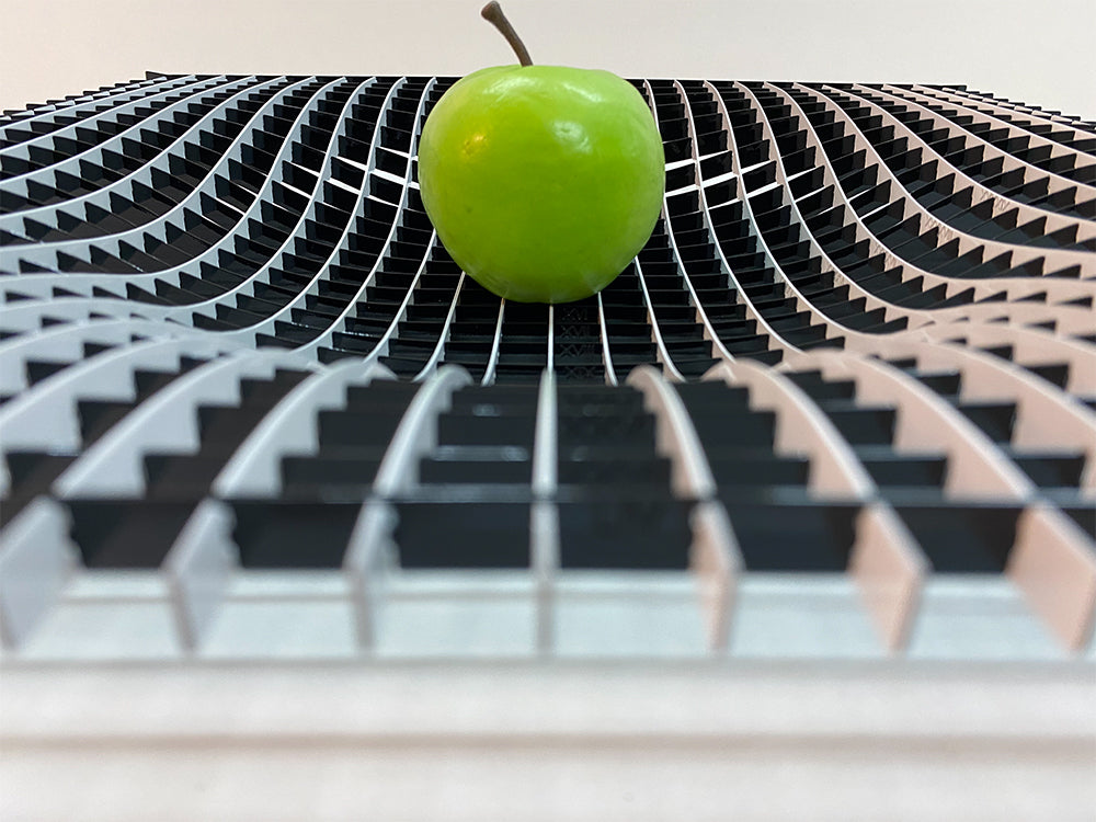 Vooraanzicht van de Gravity fruitschaal met golvend metalen rooster en groene appel