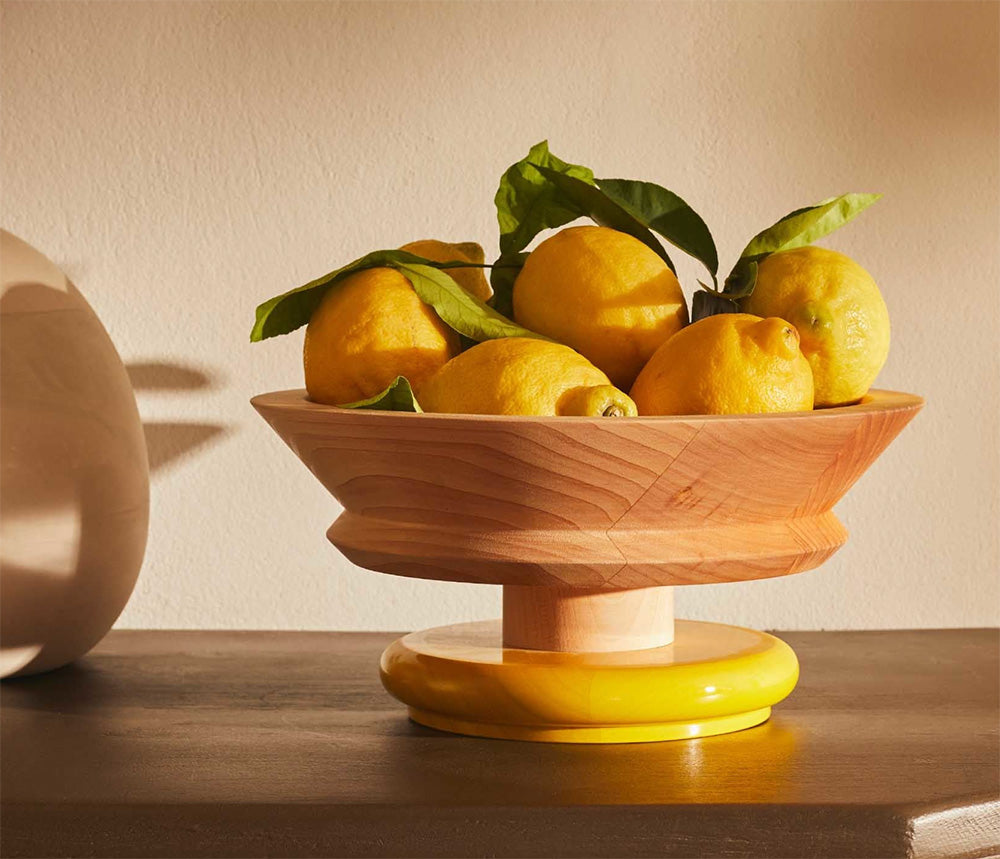 Alessi Twergi fruitschaal in blank hout met gele basis, gevuld met citroenen.