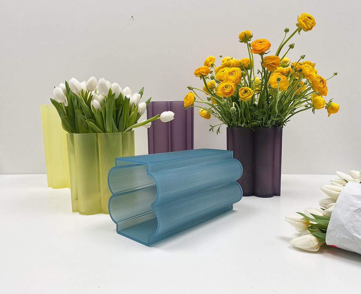 Kartell Okra vaas liggend in lichtblauw, met andere kleurvarianten op de achtergrond