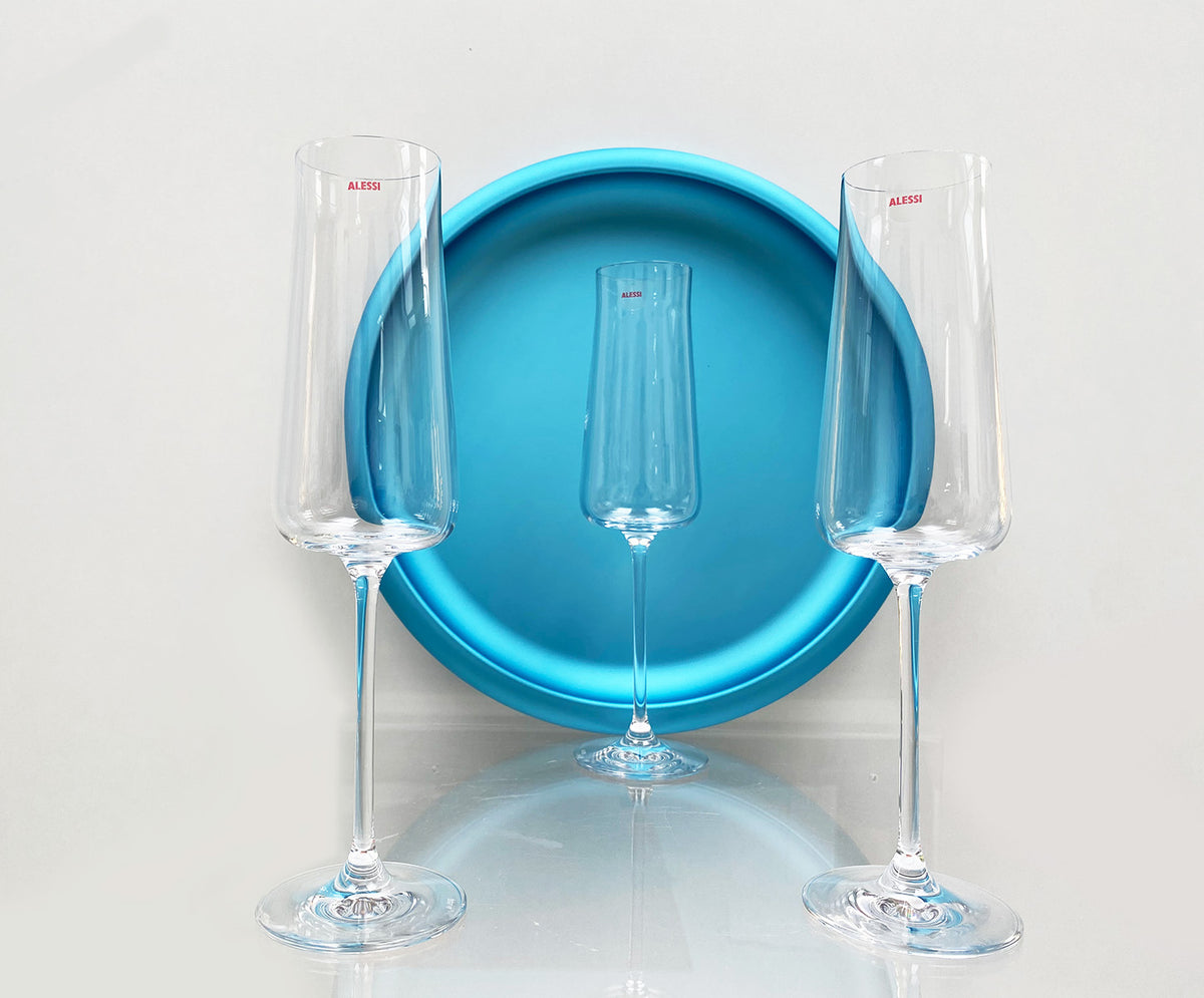 Twee Alessi Eugenia flutes van glas naast een ronde blauwe schaal.