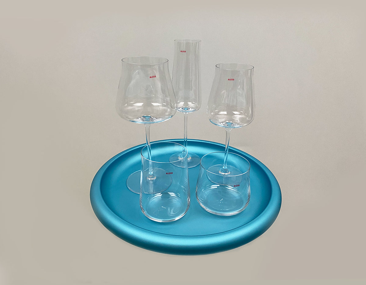 Alessi Eugenia flute en wijnglazen uit het nieuwe glas-servies op een blauwe schaal, bovenaanzicht.