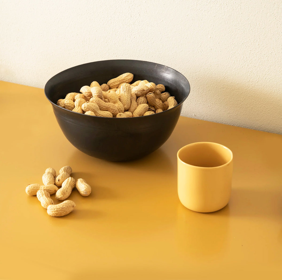 Coppa Camuna steel bowl filled with peanuts, next to yellow mug
