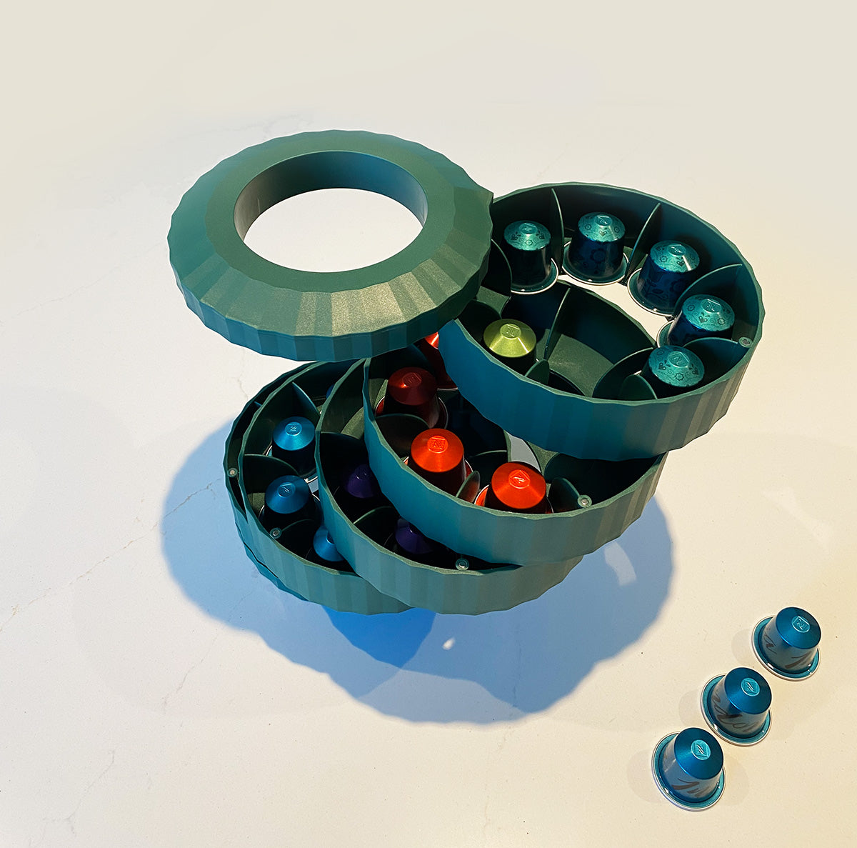 Plissé capsulehouder van Alessi in groen, geopend met losse capsules ernaast