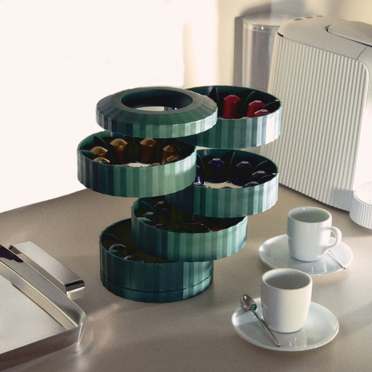 Plissé capsulehouder van Alessi in groen, in gebruik naast koffiekopjes en machine