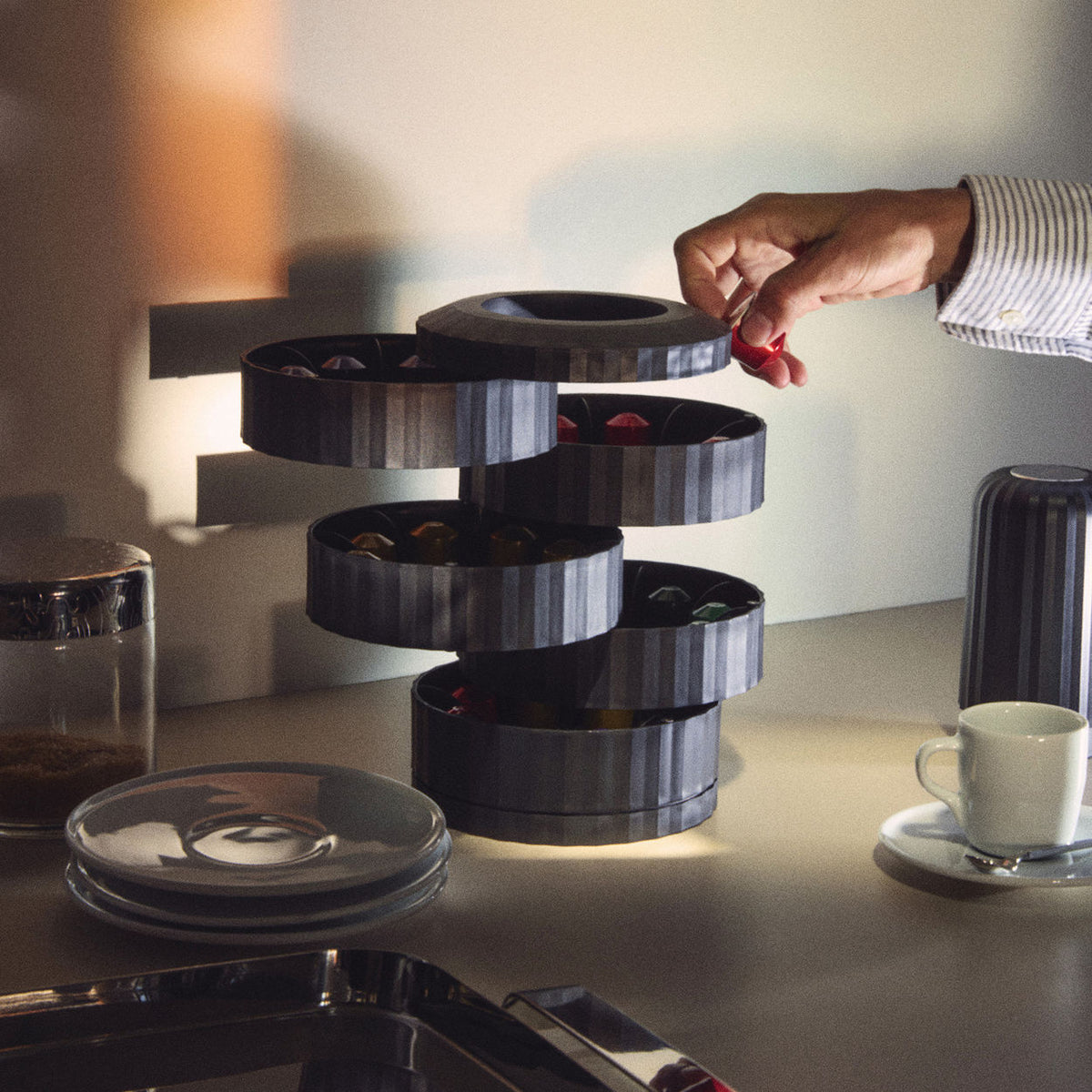 Alessi Plissé capsule holder in black, hand taking capsule from open compartment