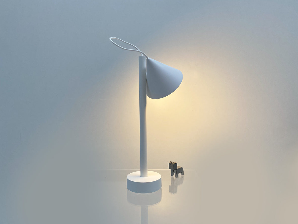 Tsumiki tafellamp van Alessi in wit, brandend met kap omhoog gericht op de staaf