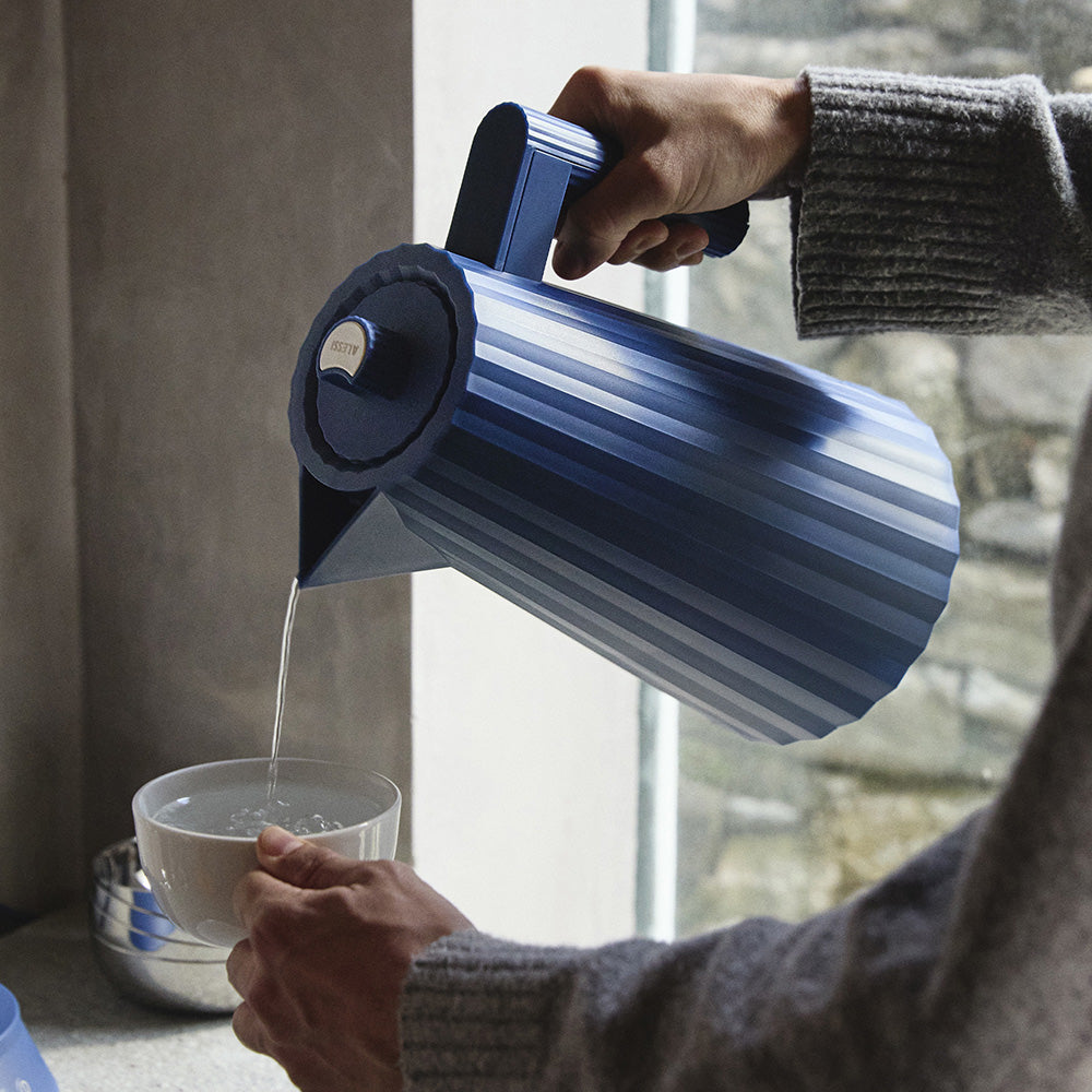 Plissé waterkoker van Alessi in blauw, in gebruik tijdens het inschenken van water