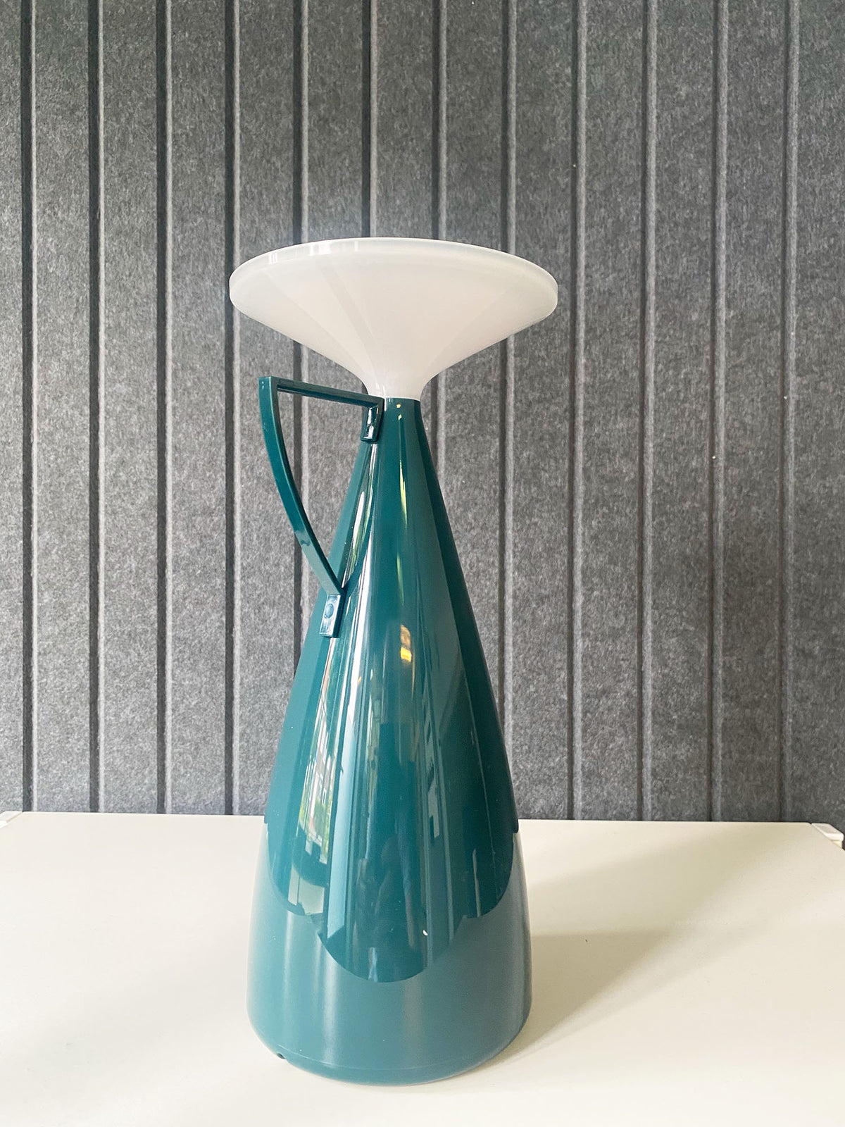 Camomille table lamp in petrol, front view against a grey wall
