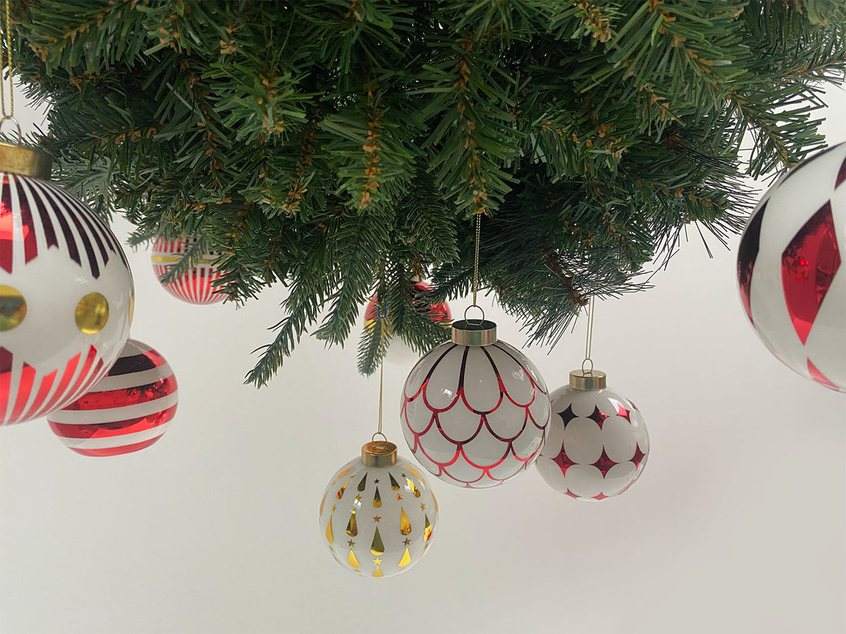 Detail van kleine glazen kerstballen met rode en gouden motieven, hangend tussen takken