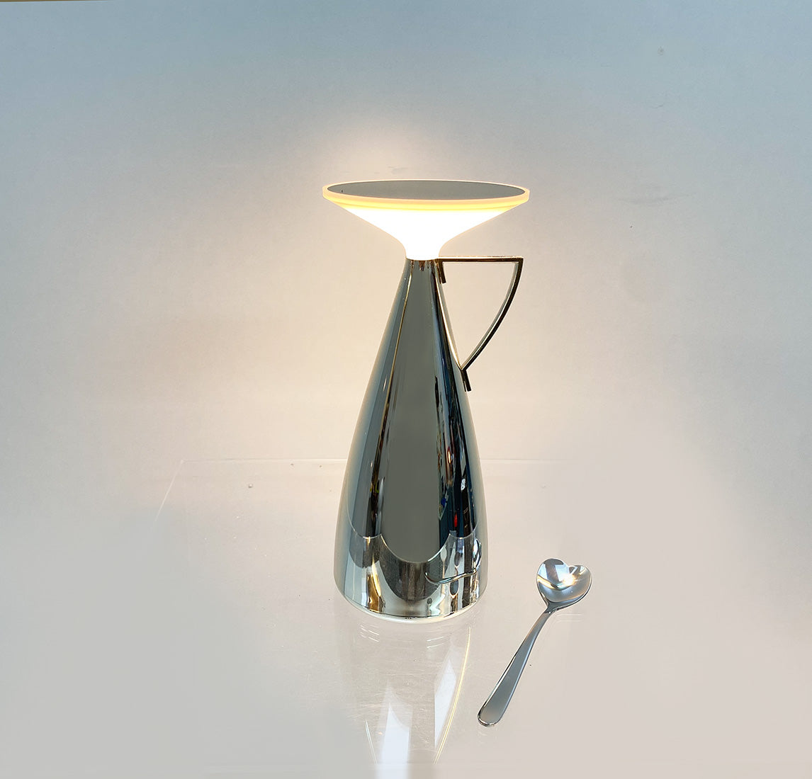 Camomille tafellamp van Kartell, brandend, naast een lepel