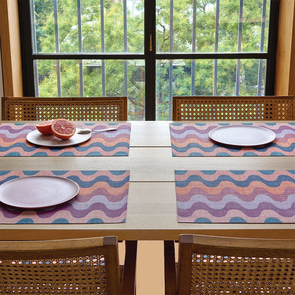 Four Chilewich placemats in pink, orange and blue tones, table with plates and fruit