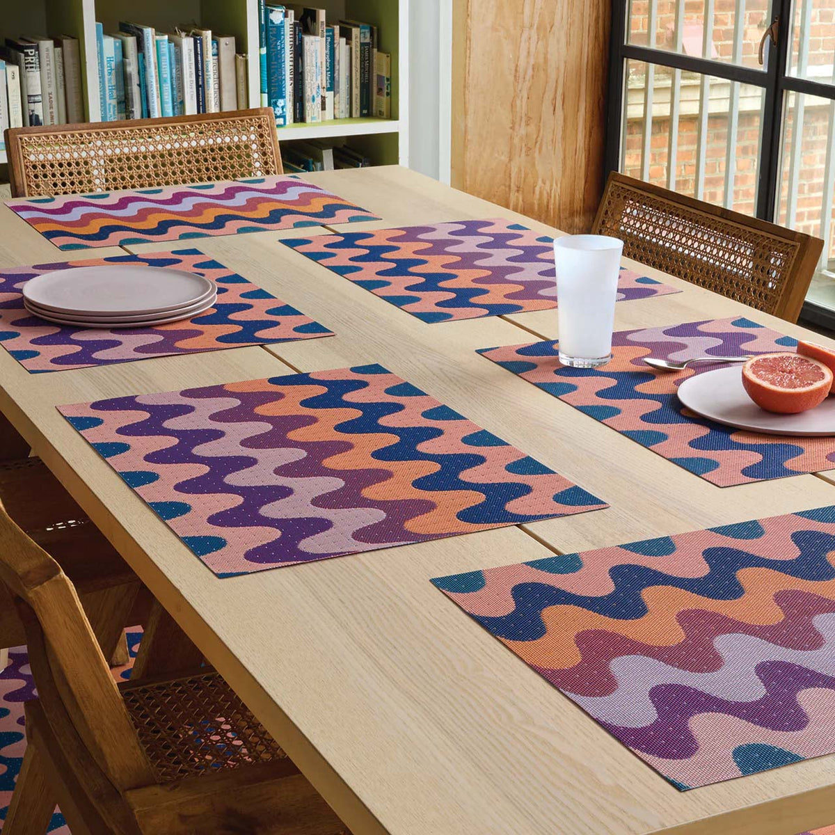 Set of Chilewich placemats in pink, orange and blue tones on set dining table