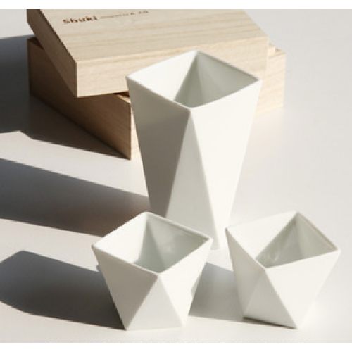 Drie Shuki sake-kopjes van Alessi, wit keramisch, naast de houten verpakking