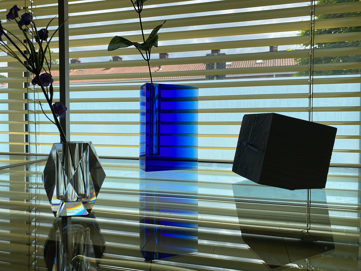 Alessi Rainbow kleine vaas in blauw, naast een zwarte kubusvorm