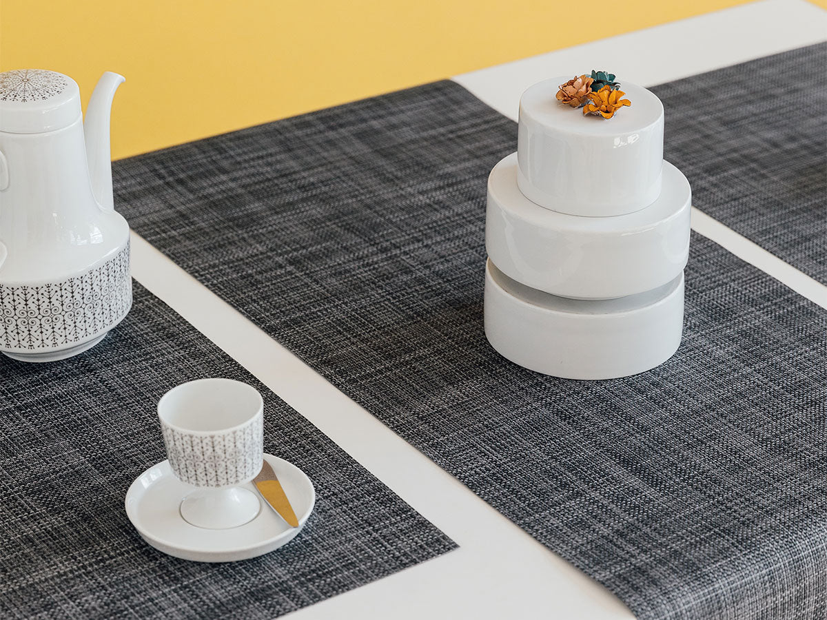 Beautiful grey placemats on table with teapot, cup and saucers