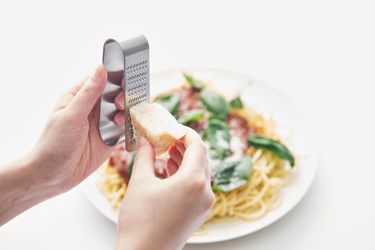 Oros Handy kleine rasp in gebruik, kaas raspen boven een bord pasta.