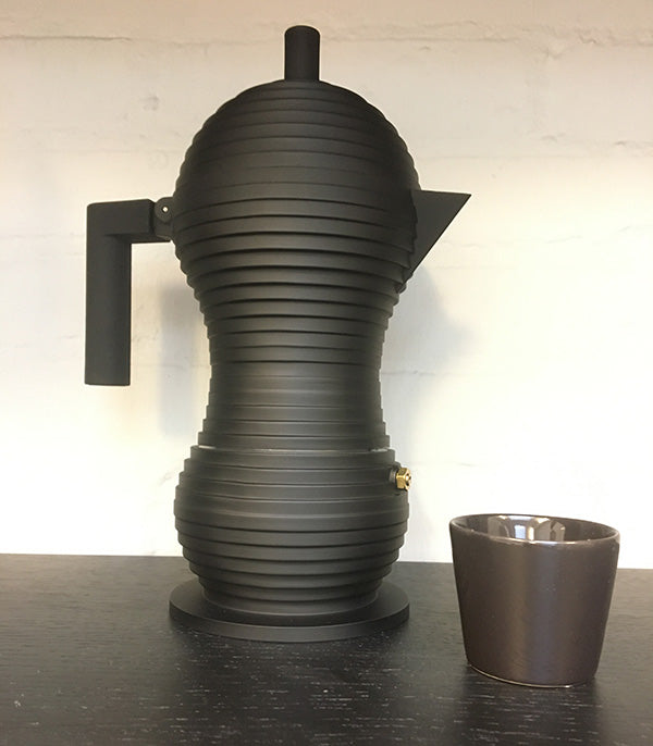 Alessi pulcina espresso maker in black, 6-cup, next to espresso cup