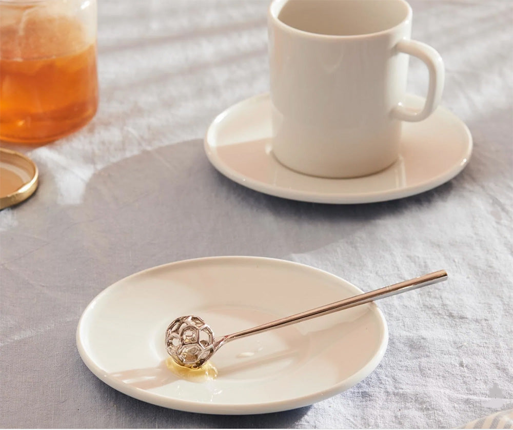 Alessi honey spoon on saucer next to tea mug and honey pot