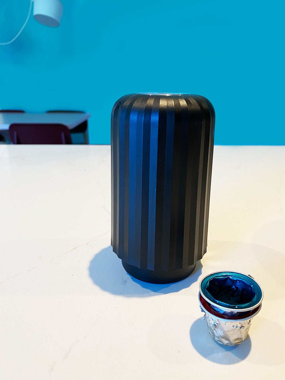 Plissé capsulecrusher in zwart, staand naast beker met gecrushte capsules