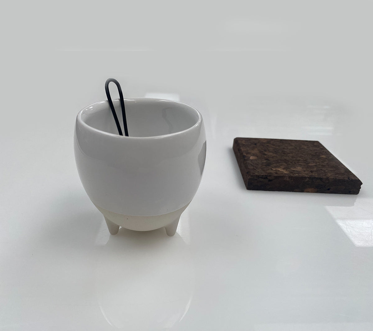 Alessi Egg Coffee Cup met ronde bodem, wit met mat zand, kurken onderzetter naast het kopje