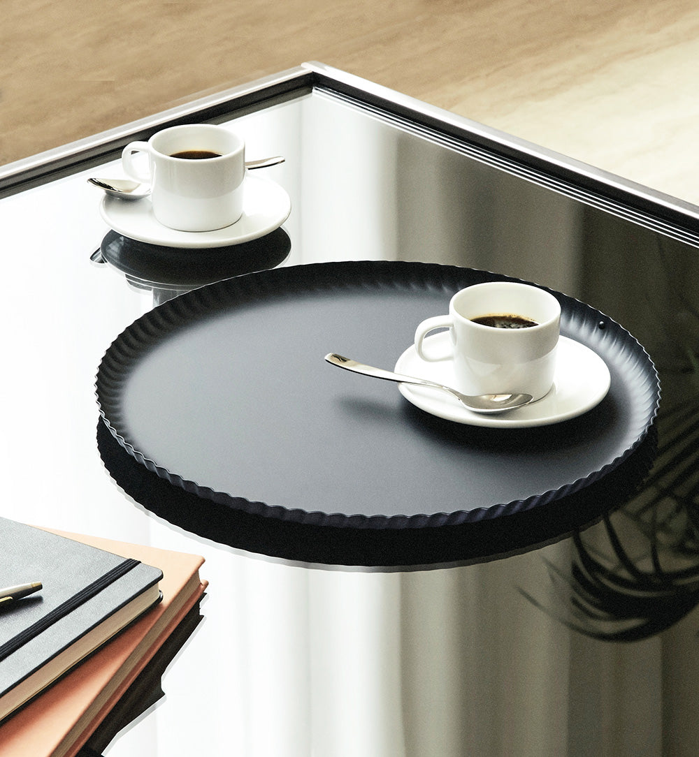 Rond dienblad uit de Pleats-serie van Alessi, zwart, in gebruik met koffiekopjes.