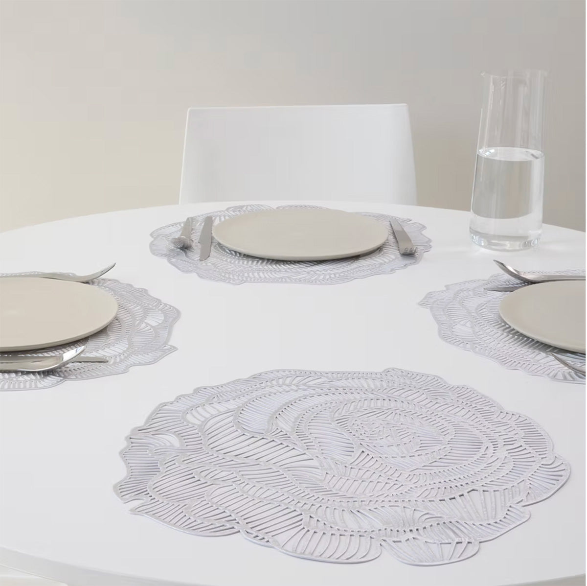 Placemats in gebruik, elk met bord en bestek, opengewerkt roosmotief in zilverkleur.