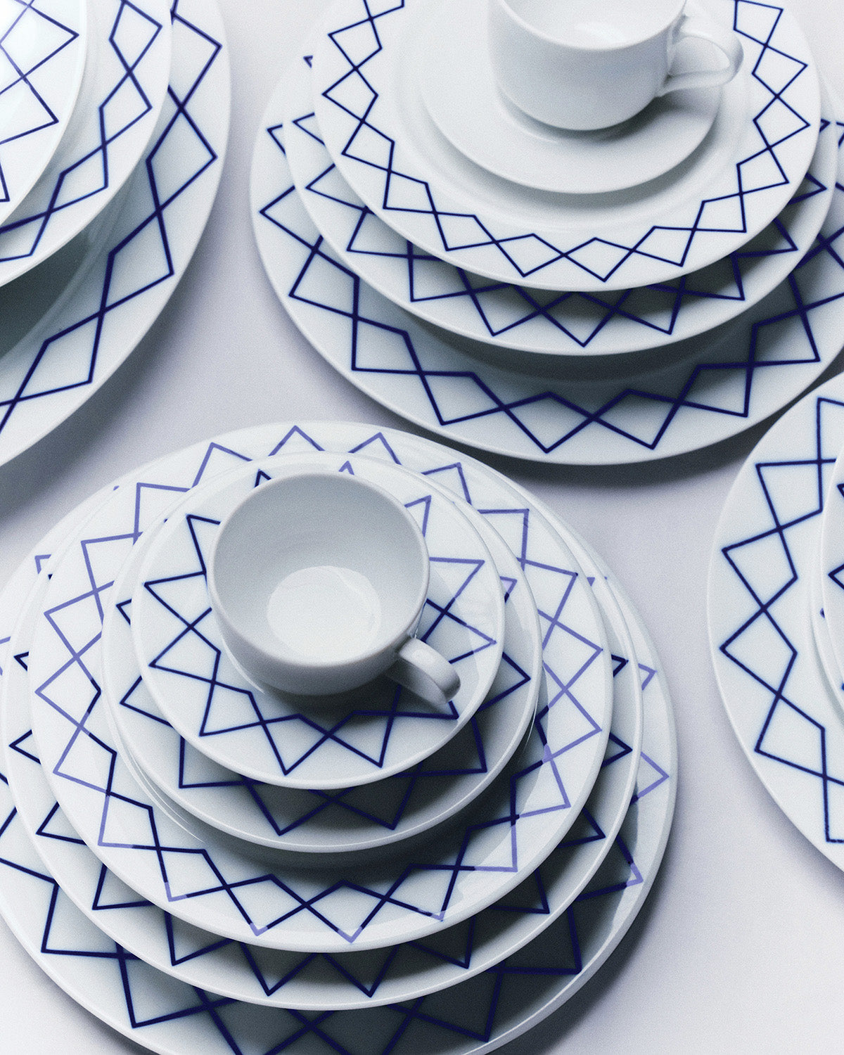 Detail van gestapeld servies met groot schoteltje, blauwe geometrische decoratie op wit
