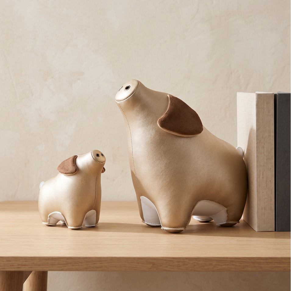 Zuny Pig Diya paperweight and bookend in pearl gold next to books on a wooden shelf
